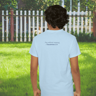 Man facing a fence wearing a blue shirt. The back says "Pray without ceasing - 1 Thessalonians 5:17"