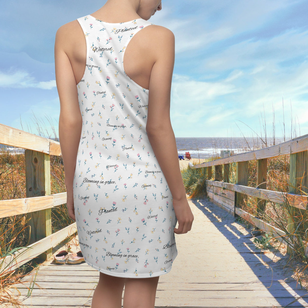 Back of woman wearing racerback white dress with small flower print and words that say "Blooming in Grace", "Planted", Watered", and "Growing".