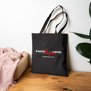 Woman holding a black tote bag with 'Faith Hope Love' text on a white background