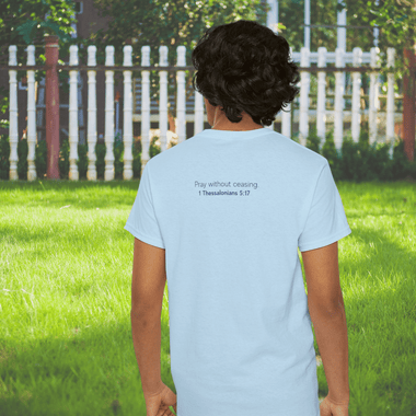 Man facing a fence wearing a blue shirt. The back says "Pray without ceasing - 1 Thessalonians 5:17"