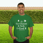 Man wearing a green t-shirt with 'Go Outside & Seek God' text, standing in a grassy area with a wooden fence and greenery.