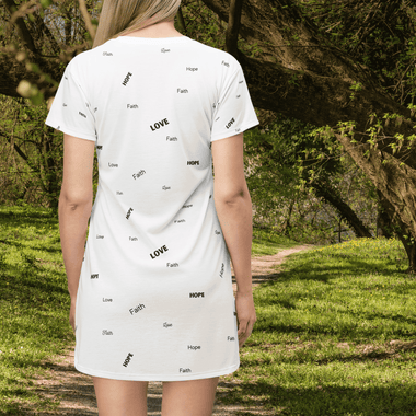 Woman wearing a white tunic back view with nature scene in back. Tunic has the words "Faith" "Hope" and "Love" printed in all directions all over the top.